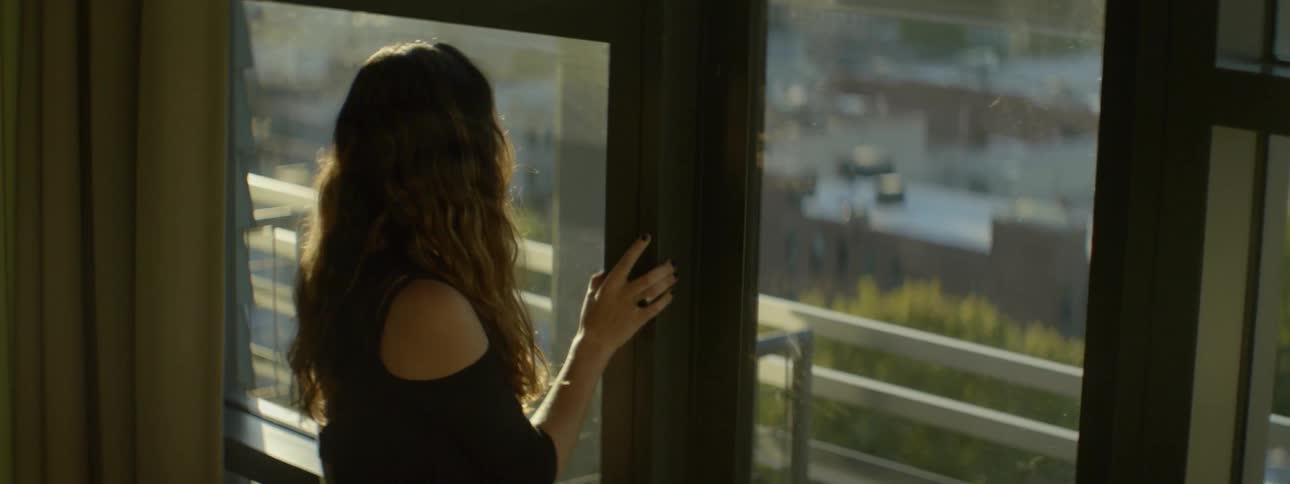 A woman looks out of a window at a city