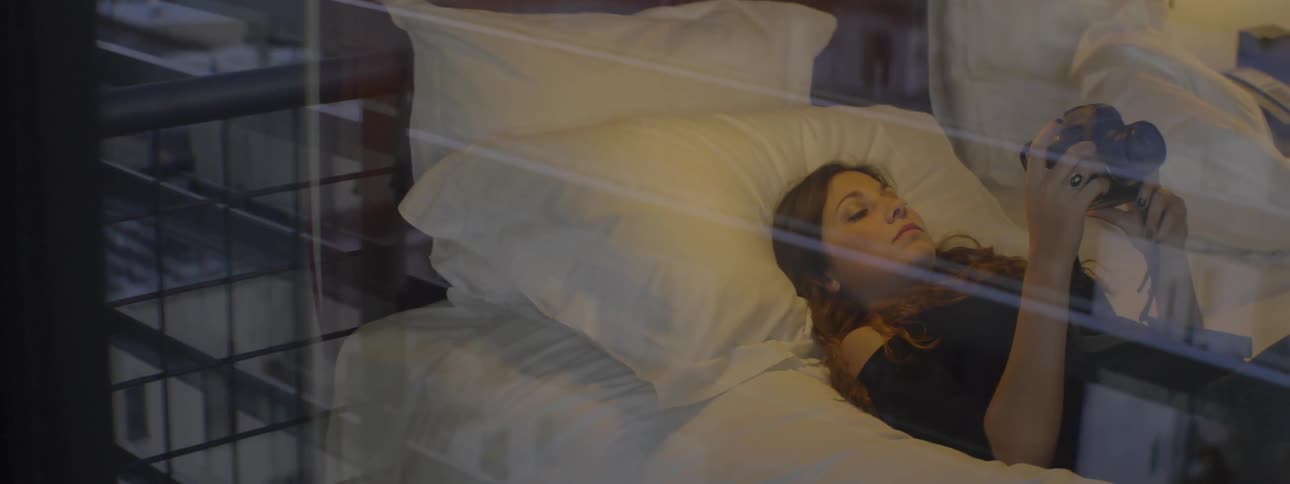 A woman lies on a bed looking at a camera