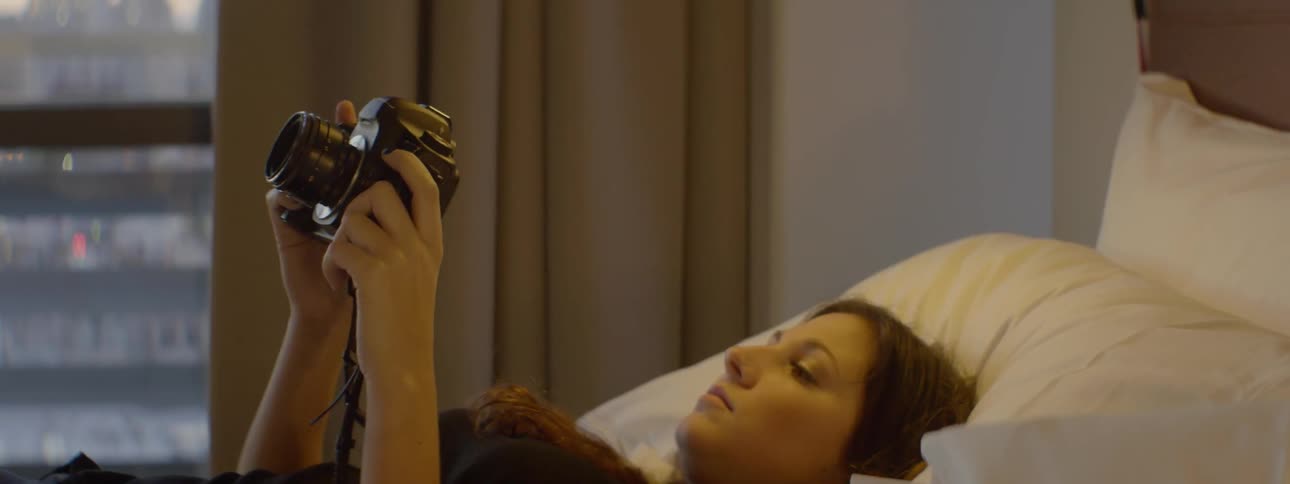 A woman lies on a bed fiddling with a dslr