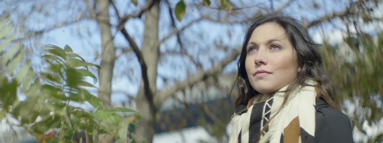 Woman wearing a multi-colored scarf stands beside a bush