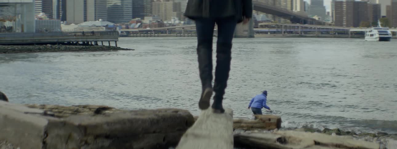 Close up of a person walking over a log with a city behind her