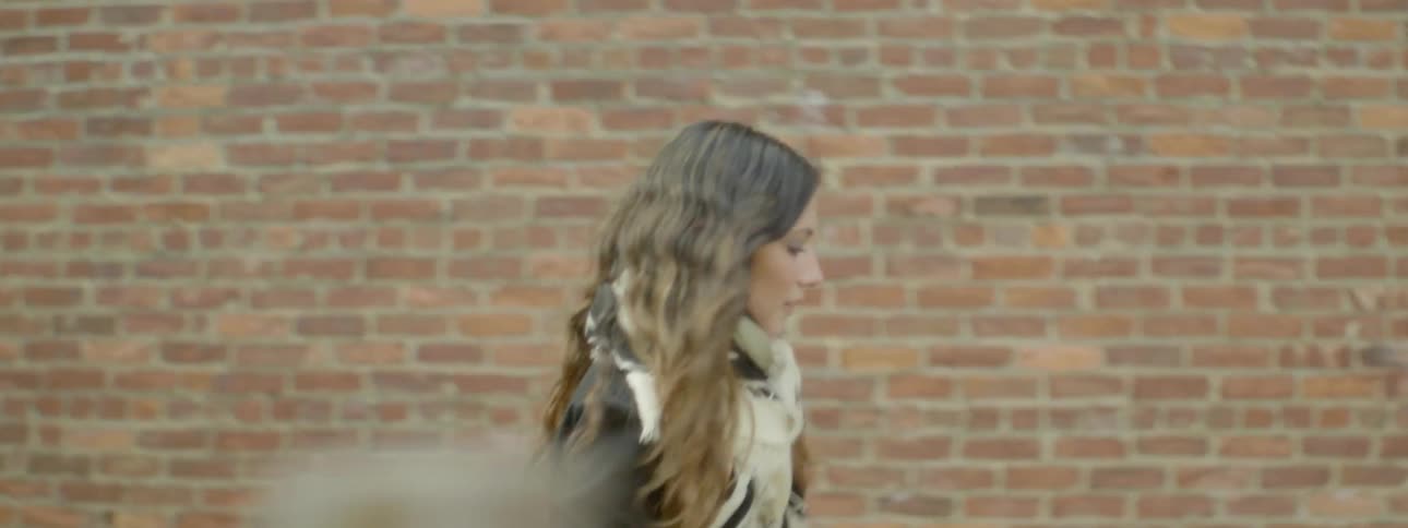 A woman is walking outside past a brick wall