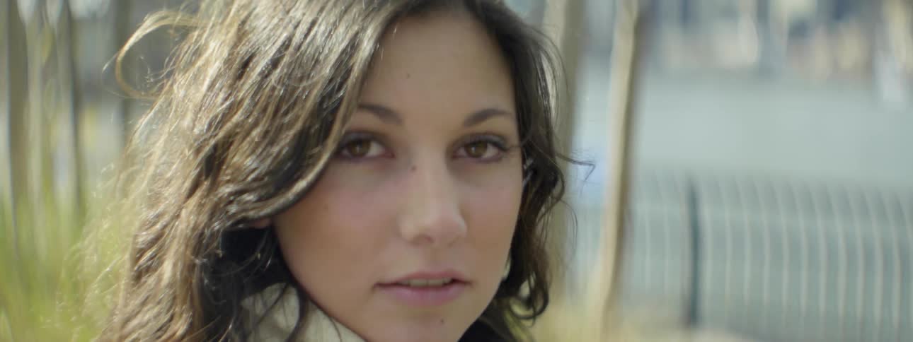 A woman wearing a scarf and standing outdoors turns and looks at the camera