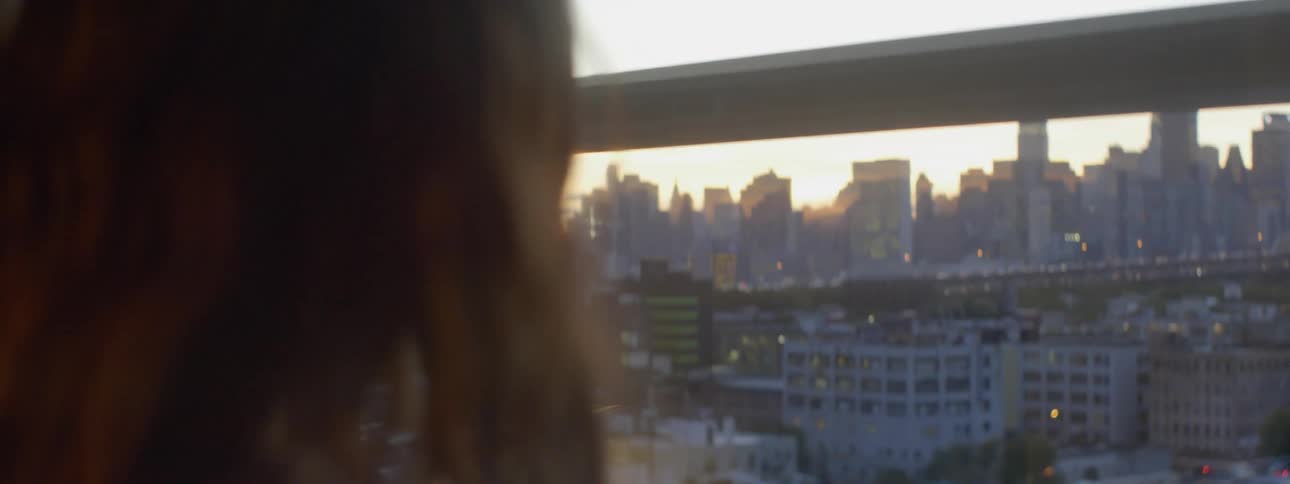 A dark haired woman looks out a window into the city