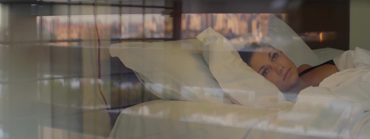 A woman lies in bed and looks out of the window