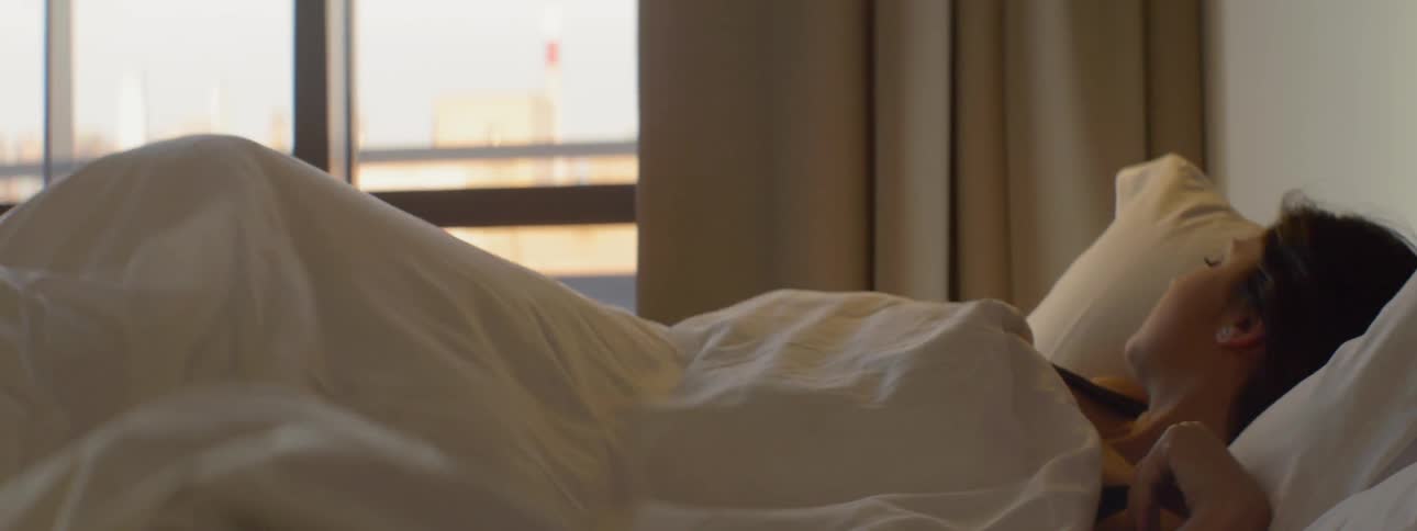 Woman in bed with covers rolling over to look out the window