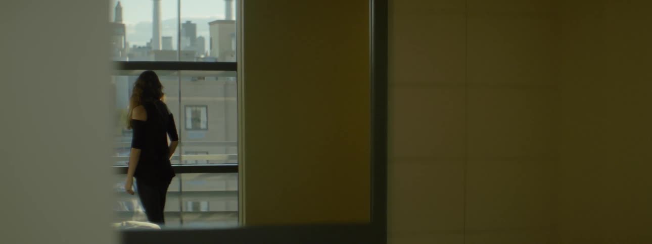 A woman in a black shirt turns away from a window