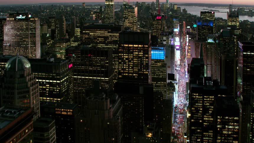 Neon lights and screens flash over heavy traffic through downtown with river and red sky in background