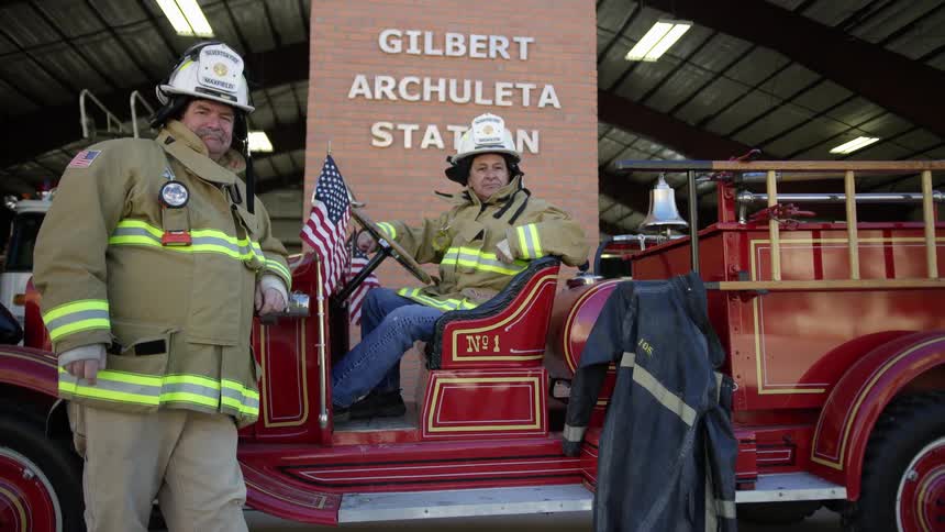 Two firefighters pose on an antique fire truck