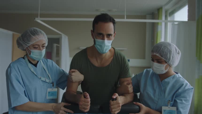 Nurses flank both sides of a patient as they help him walk with use of a leaning apparatus