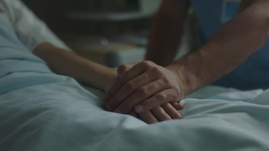 Doctor puts hand over a patients hand laying on the hospital bed