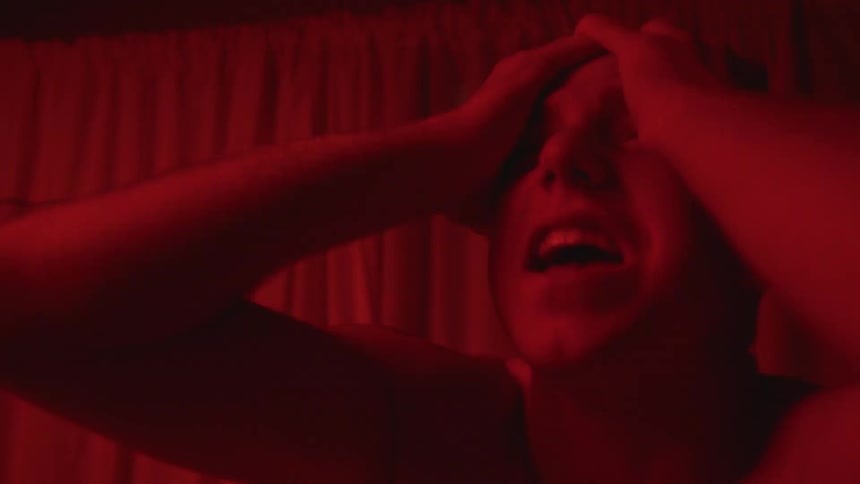 Man stands yelling near windows clutching his head under red colored lights