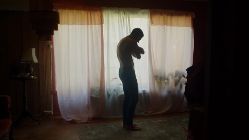 A man standing in a room with a wall a window and curtains in the background