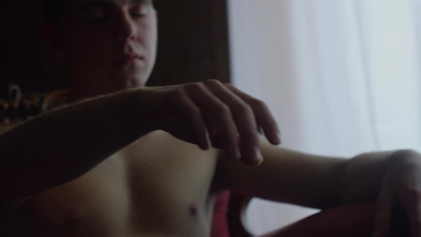 Man reaches hand forward while sitting on chair near curtained window