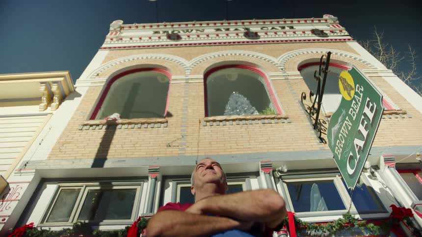 A man stands with his arms crossed outside his restaurant