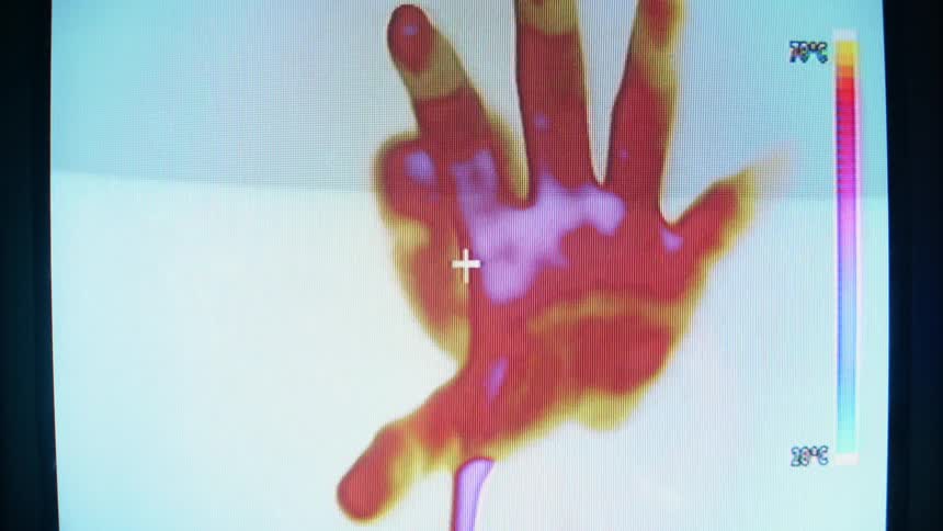 A man on the monitor is waving his hand towards the screen