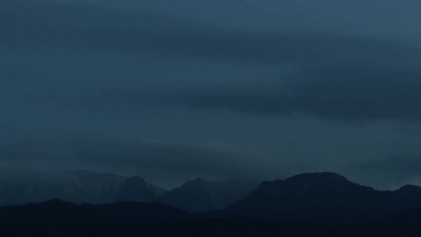 Time lapse of night falling over the mountains under clouds
