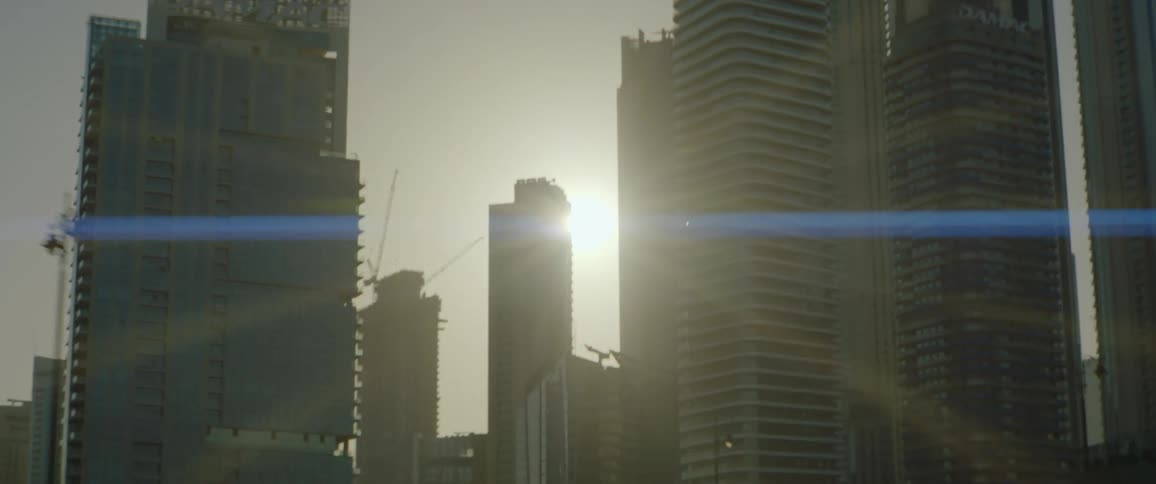 Sun shines past skyscrapers including one building under construction by cranes
