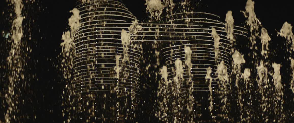 A large fountain shoots water up in front of the building at night