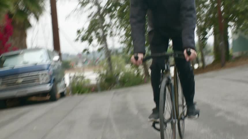 A man gets onto a bicycle and starts peddling and riding in a parking lot