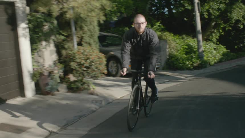 A man rides his bicycle down the middle of a crowded neighborhood street