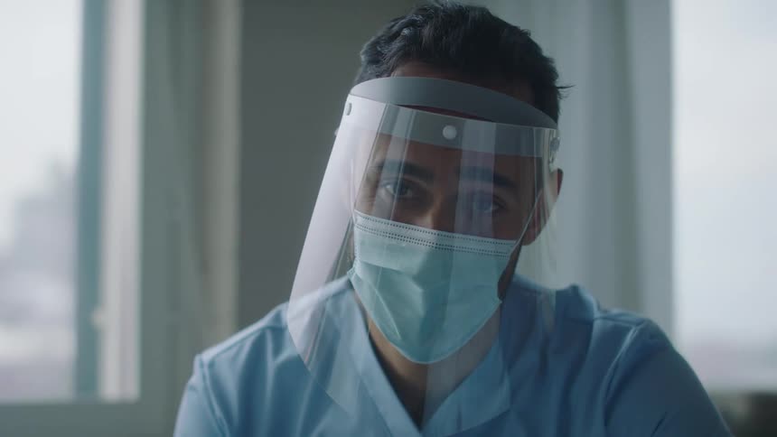 Doctor wearing face mask and shield talks to a patient and gets up
