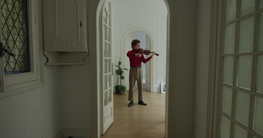 Young man wearing red shirt playing the violin at home