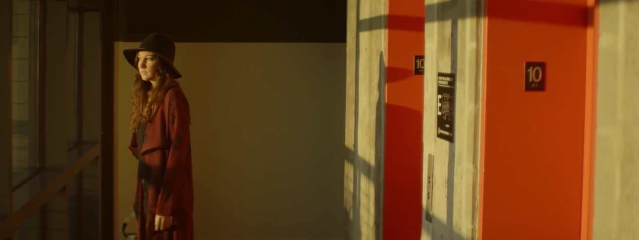A woman wearing a purple jacket stands near a door