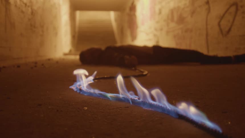 A person laying down in a corridor with a wire on fire in the foreground with a wall and stairs in the background