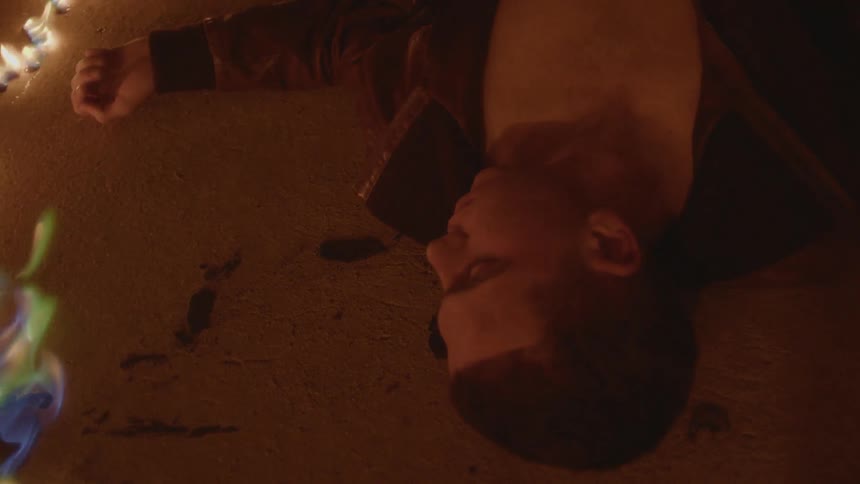 Man lies unconscious on floor surrounded by flames injacket showing his bare chest