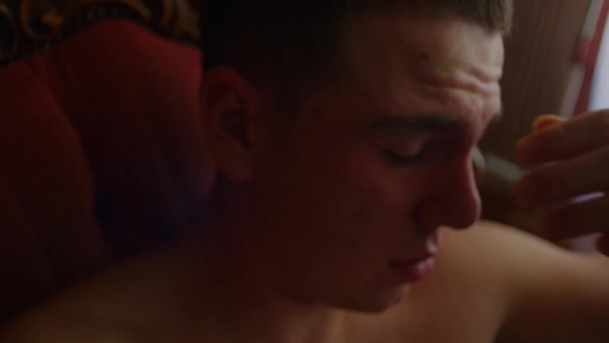 Young shirtless man sitting on a chair rubs his eyes shaking his head in pain