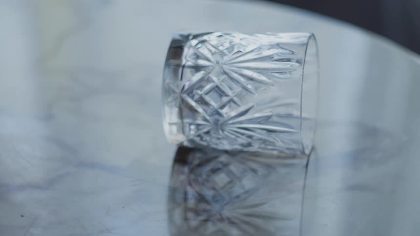 The smooth marble surface of a round table reflects a tipped over glass