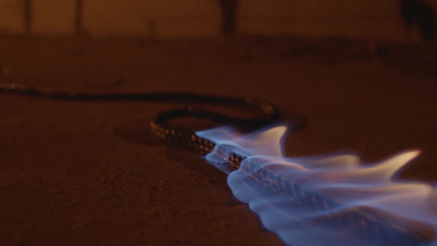 An electrical cord on a floor is on fire and the flames are moving across the floor