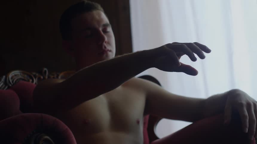 A man in a room sitting on a couch with a wall and window in the background