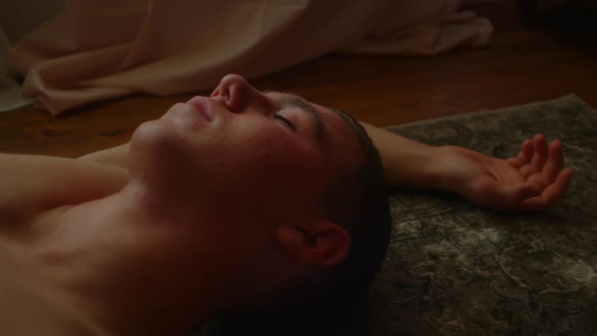 Shirtless man lies down on the ground with eyes closed in the living room at home
