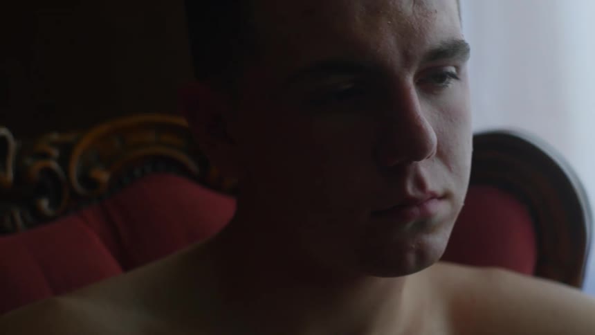 A sad looking man is sitting in a chair in a room and staring off