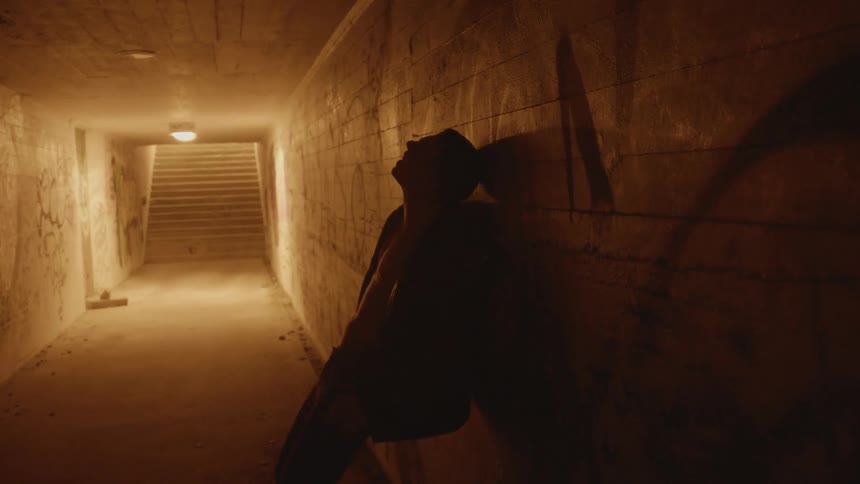 A man stumbling in a corridor with graffiti on the walls with stairs in the background