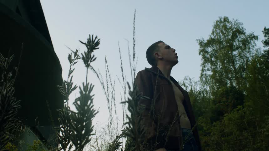 A man standing in front of a house with trees the sky and clouds in the background