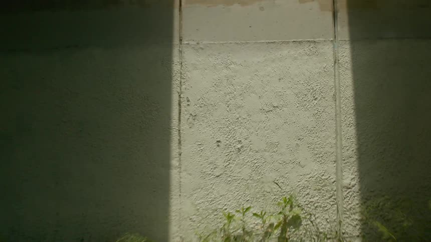 A sidewalk next to a wall with a person on a bicycle riding by