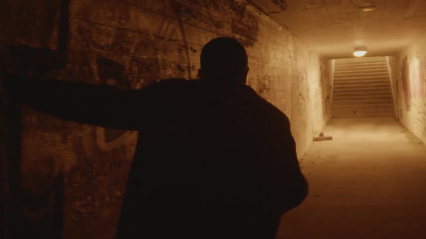 A man stumbling and falling in a corridor with graffiti on the walls with stairs in the background