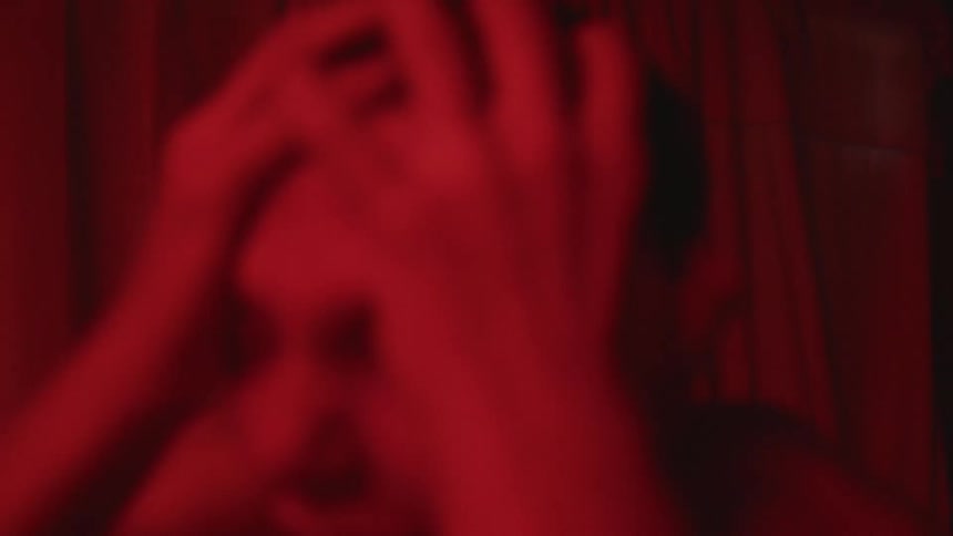 Young shirtless man screams in pain holding his head inside a dark room under red strobing lights