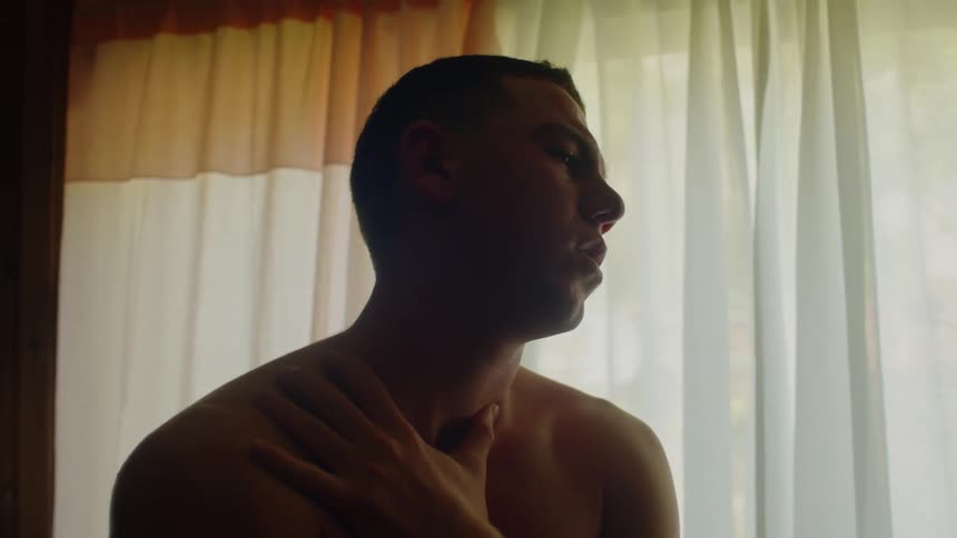 A man is standing in front of a window rubbing his neck