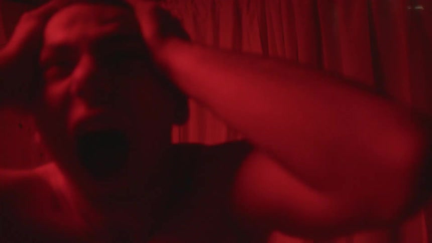Shirtless distressed man screaming in a room under flashing lights