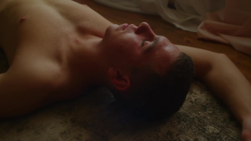 A shirtless man asleep on a floor with one arm above his head