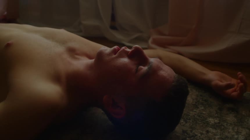 A man in a room laying on the floor on a rug with a window and wall in the background