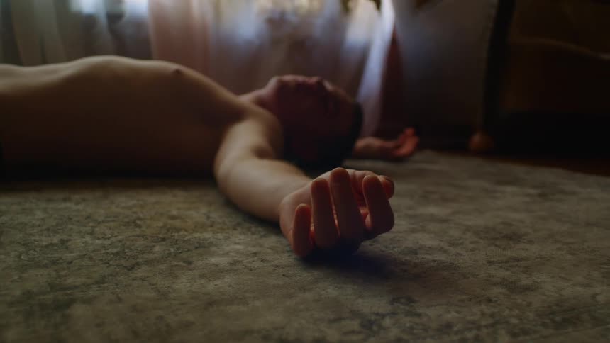 Shirtless man laying on the carpet unconscious in a room