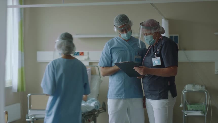 Nurses talking to each other in front of a patient laying in bed on a hospital room