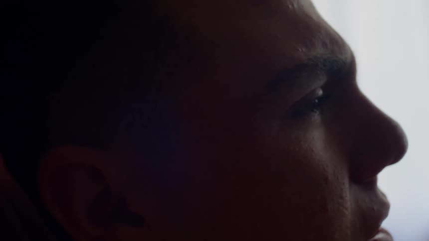 Close up of the face of a sad young man inside a dimly lit room at home