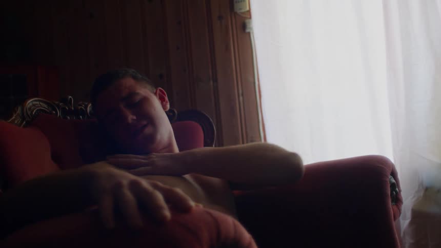 Uncomfortable young shirtless man sitting on a red chair shakes and wiggles