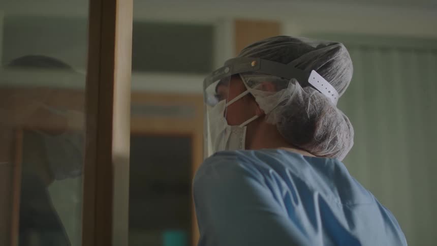 Nurse wearing personal protective gear opens the door of a hospital room